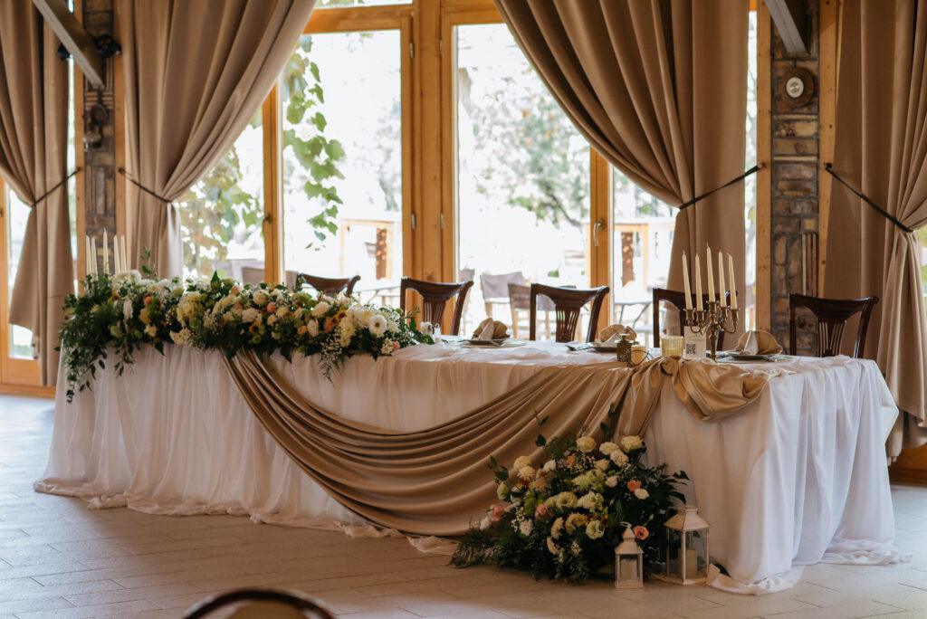 Mladenački sto dekorisan za svadbu sa cvetnim aranžmanima i elegantnom dekoracijom u sali